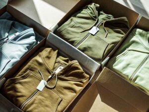 Variety of zip hoodies in earthy tones packed in open boxes with hangtags.
