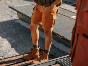 Man in rugged orange cargo shorts and boots outdoors on sunny day.