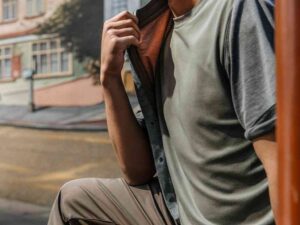 Man wearing layered t-shirts with jacket, seated in cityscape
