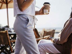 Woman in grey joggers holding coffee during sunny cafe outing