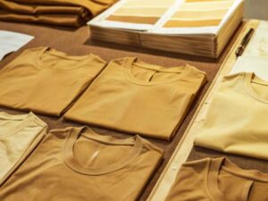 Flat lay of folded earth-tone T-shirts beside matching swatch book