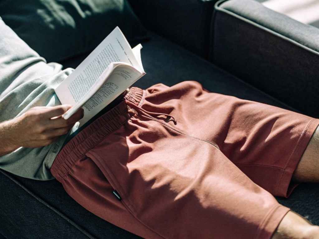 Man lounging on couch in relaxed fit red lounge shorts.