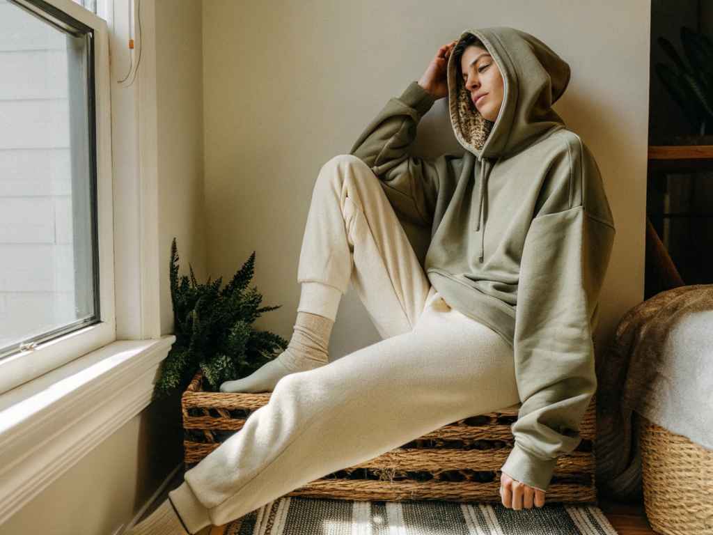 Woman in hooded sweatshirt and fleece joggers relaxing by window