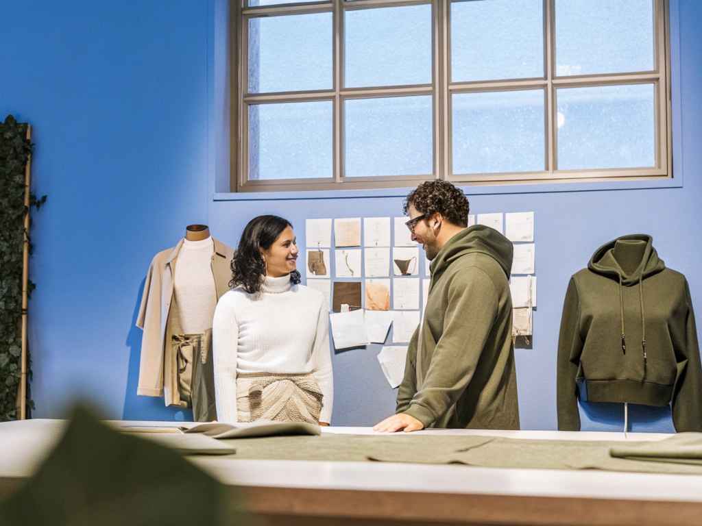 Hoodie brand founders discussing designs in studio with mood board and mannequins.