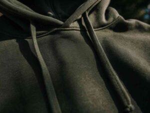 Close-up of dark green hoodie fabric and drawstrings in sunlight