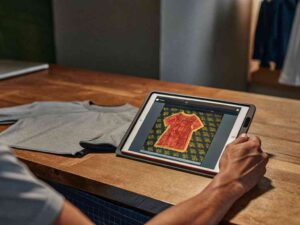 Person editing shirt design on tablet with grey t-shirt on table