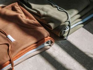 Folded hoodies in brown, orange, and olive green on concrete floor