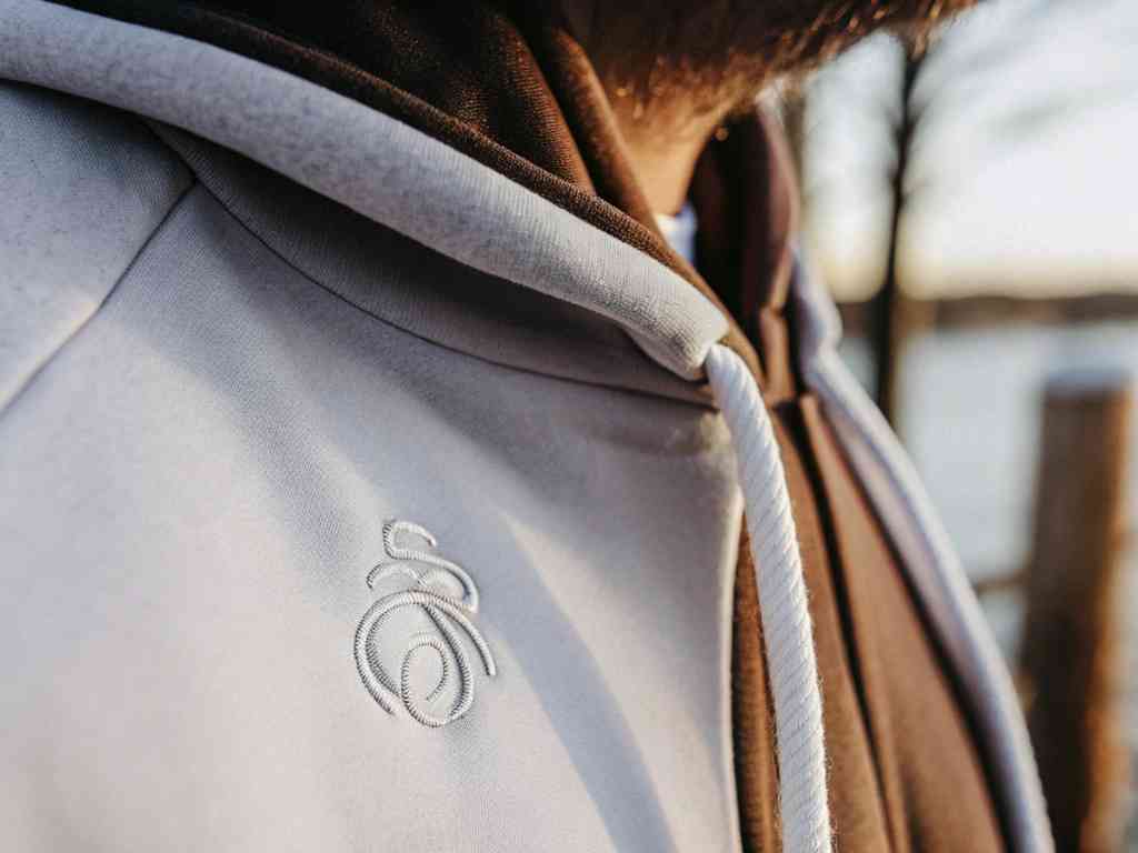 Close-up of white stitched logo on gray hoodie chest