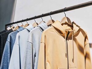 Row of custom zip-up hoodies in neutral tones hanging on rack.