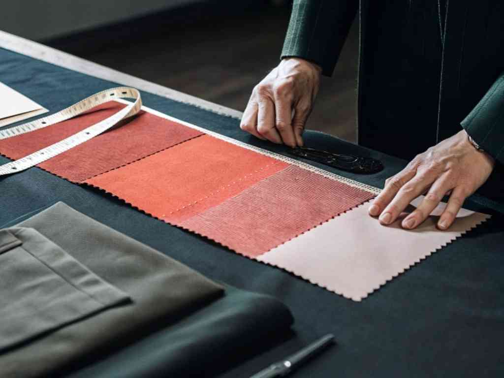 Hands arranging red and pink fabric swatches on a table with measuring tape.