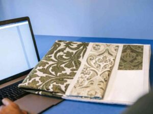 Fabric swatches with intricate designs and a laptop on a table in a creative workspace.