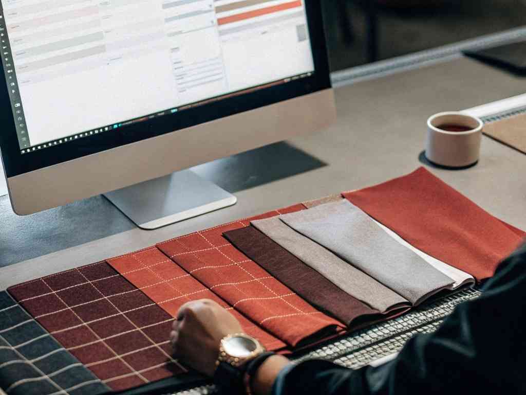 Sourcing expert analyzing fabric swatches while using a desktop with a planning interface.