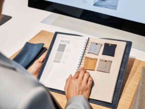 A person reviewing fabric swatches and color options in a fabric book with a computer in the background