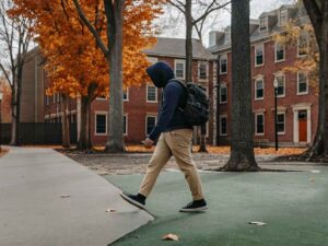 Student in hoodie walking on campus path with fall leaves