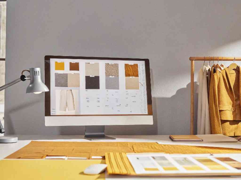 Fashion designer's workspace with color samples and clothing on screen.