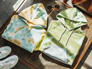 Tie-dye hoodies laid flat with sunglasses and shoes in natural light.