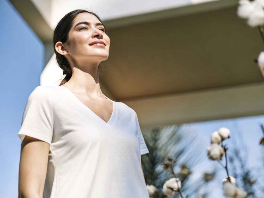 Woman in white v-neck t-shirt near cotton plants outdoors.