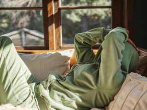 Person lounging in green hoodie set on sunny window seat