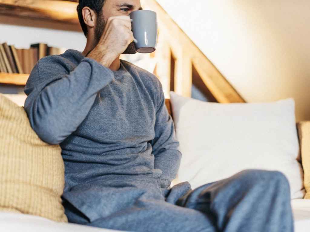 Man in grey loungewear drinking from mug on sofa