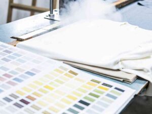 White shirt on a heat press machine beside fabric color swatch charts.