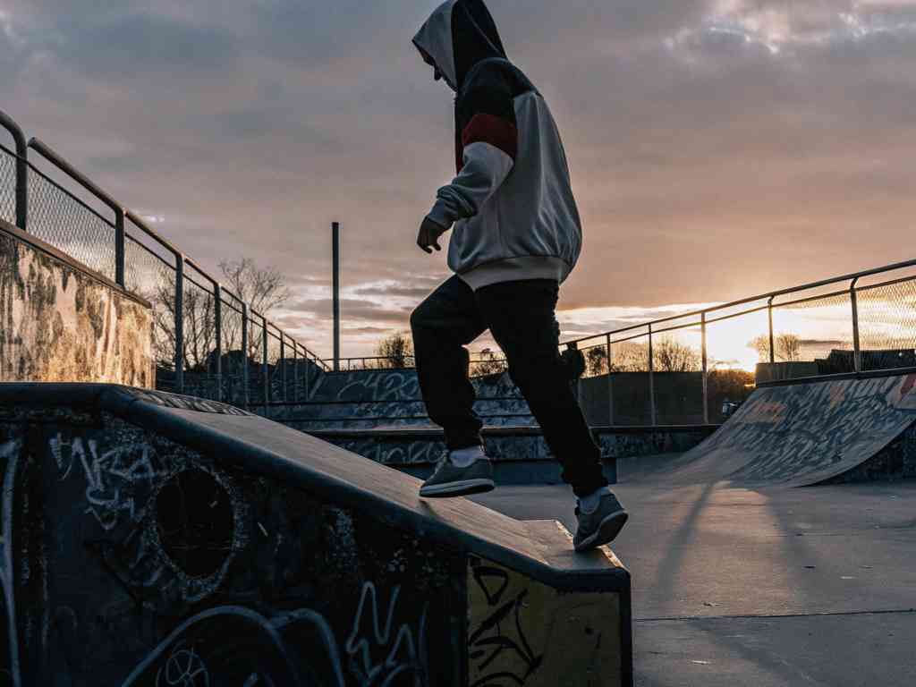 Hoodie-clad person climbing ramp at skatepark during sunset