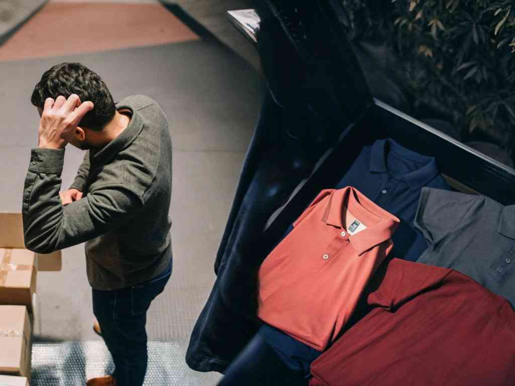 Man inspecting boxes while folded polo shirts are displayed in a suitcase.