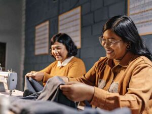 Two women smiling while sewing garments in studio