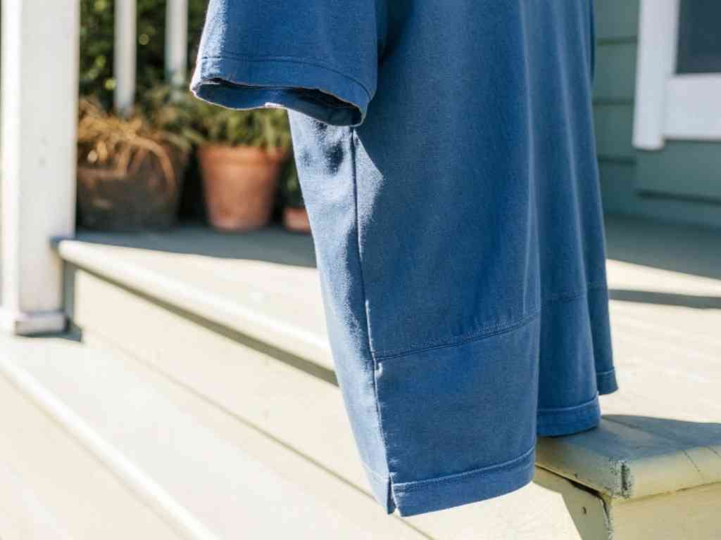 Blue short-sleeve t-shirt hanging on porch railing in sunlight