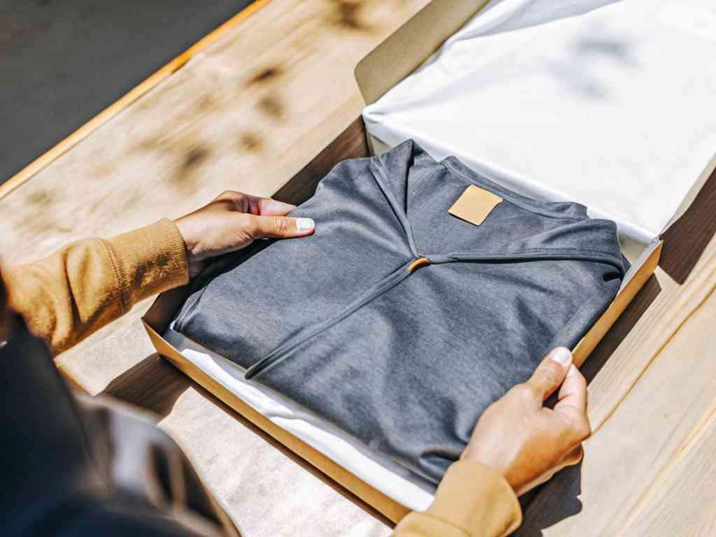 Hands unboxing neatly folded gray hoodie in premium box