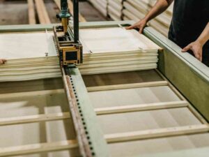 Workers using a machine to stack and arrange folded materials in a production facility.