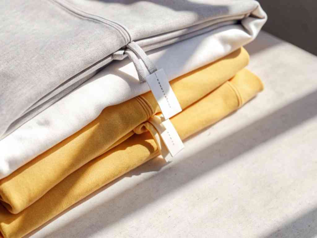 Folded gray, white, and yellow hoodies stacked on bright surface