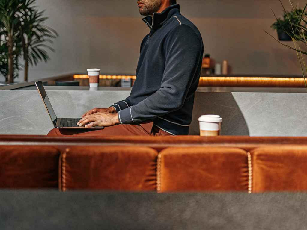 Man in navy pullover working on laptop in café