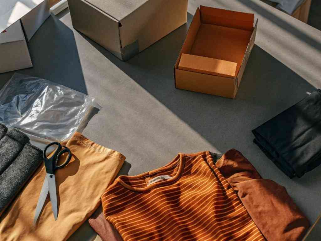 Folded clothes, cardboard box, scissors, and packaging on workspace table.