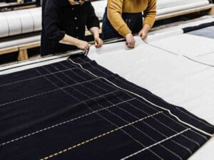 Two workers marking and measuring fabric pieces with printed patterns in a factory setting.