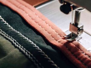 Close-up of sewing machine stitching coral trim on dark fabric