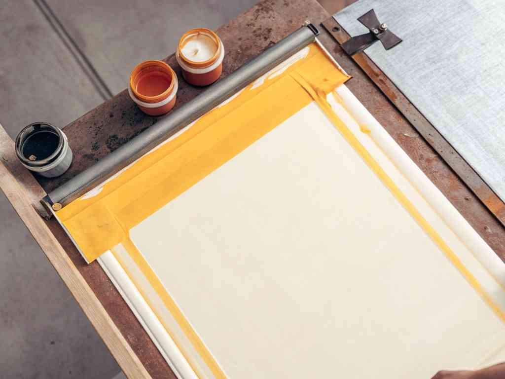 Screen printing setup with yellow tape and three jars of colored ink.
