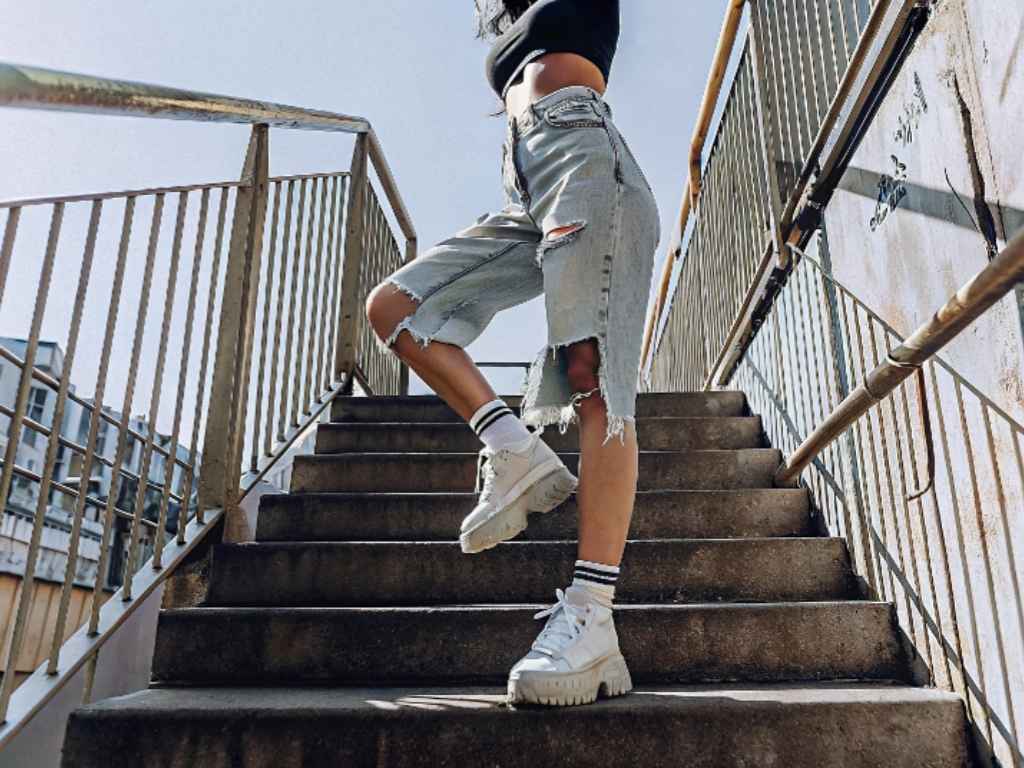 Woman in ripped long denim shorts and sneakers posing on stairway
