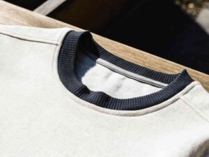 Close-up of black ribbed collar on light gray sweatshirt in sunlight
