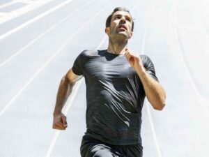 Focused male athlete running in black shirt under sunlight.
