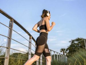 Woman running in black activewear under clear blue sky.