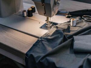 Sewing machine stitching dark fabric with thread and scissors nearby