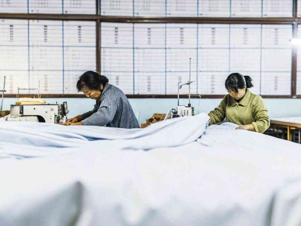 Two women working on sewing machines with fabric in a factory setting.
