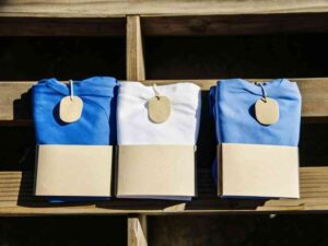 Three folded t-shirts in blue and white with blank kraft tags