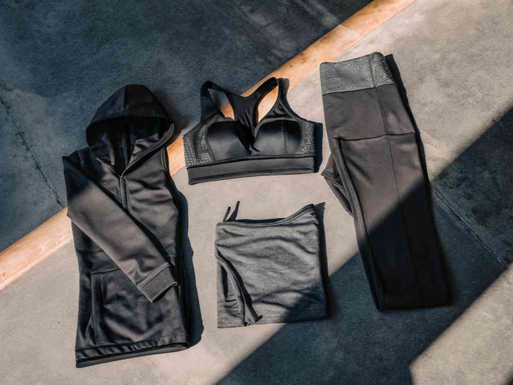 Flat lay of black hoodie, sports bra, leggings, and shorts in sunlight