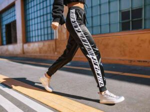 Woman walking in black joggers with bold white side text