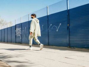 Gen Z model in oversized green hoodie walking along urban sidewalk.