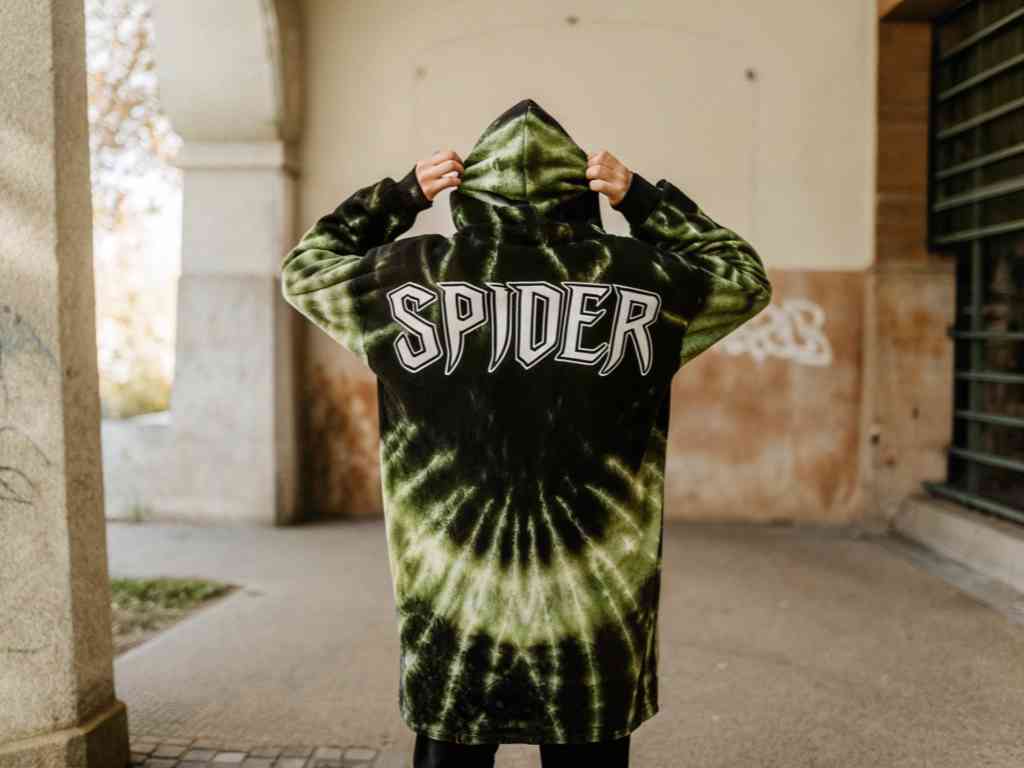 Person in green tie-dye hoodie with “SPIDER” text, adjusting hood.