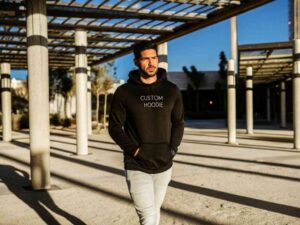 Man in black hoodie and light jeans walking in outdoor plaza