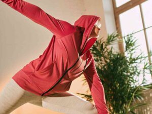 Woman stretching in red zip-up hoodie indoors