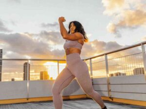 Athletic woman in mauve workout set exercising at sunrise on rooftop.